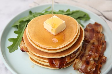 Tasty pancakes with butter, fried bacon and fresh arugula on white marble table, closeup