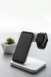 Photo of Stylish smart watch and phone charging with wireless pad on grey table
