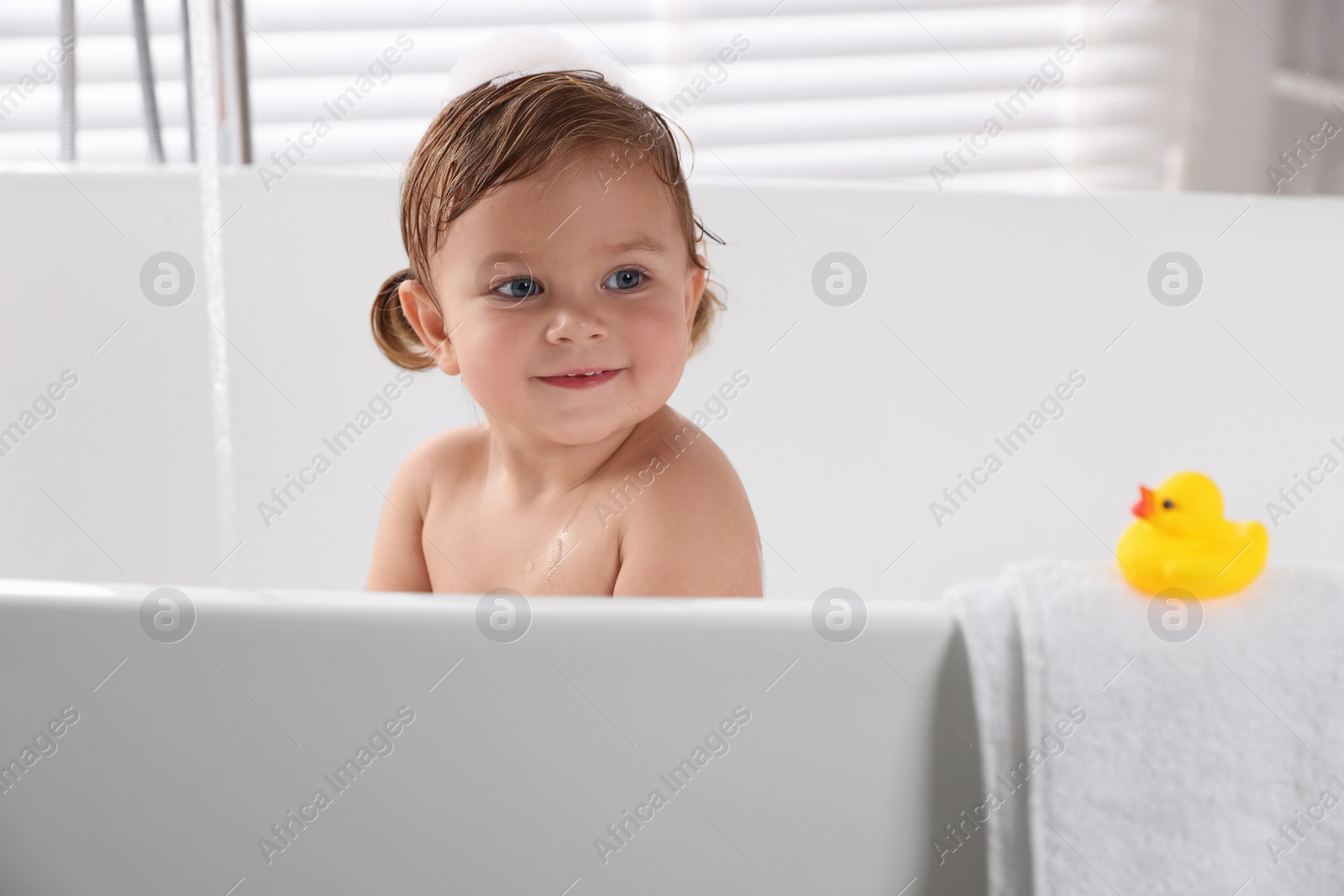 Photo of Cute little girl taking bath with toy indoors