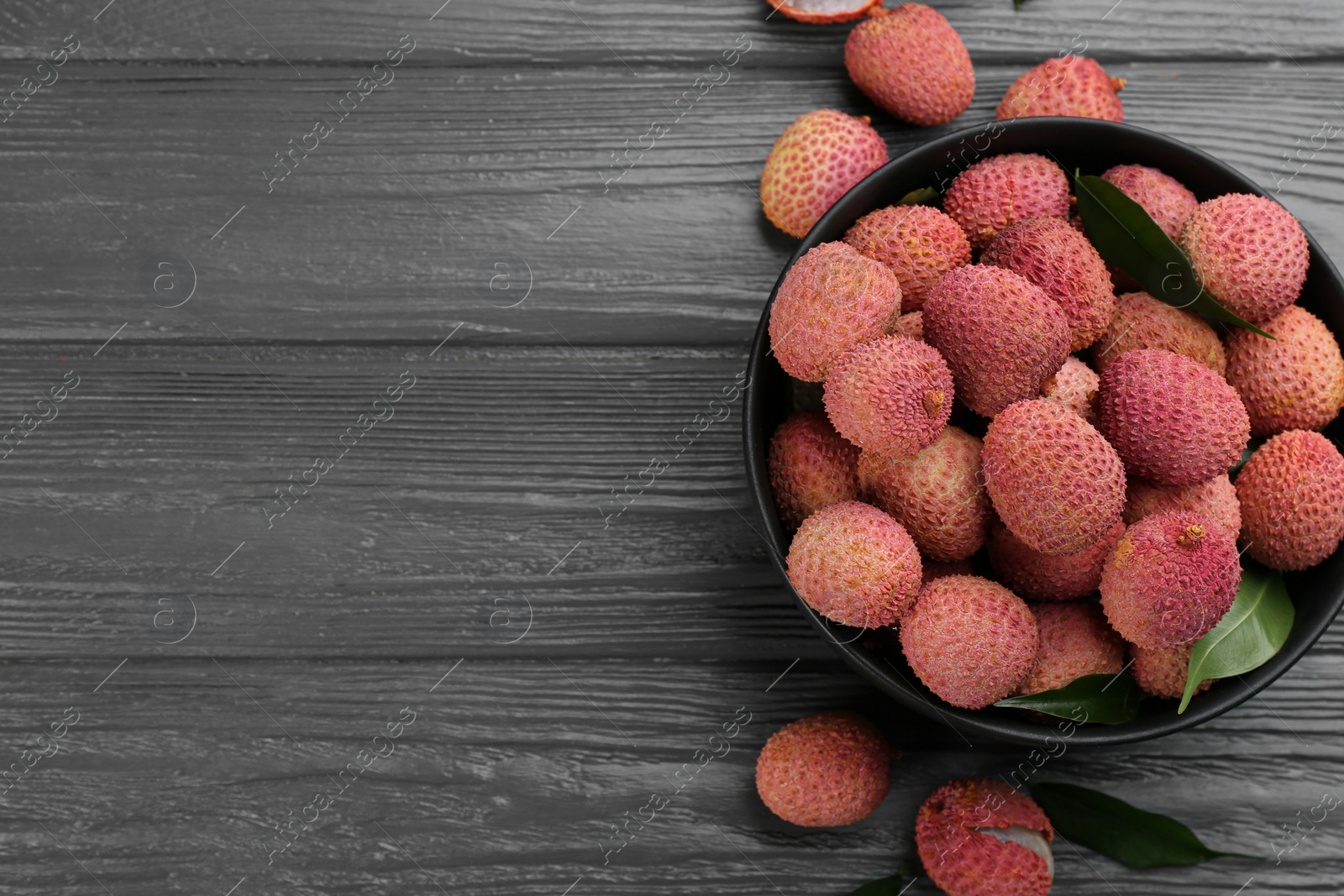 Photo of Fresh ripe lychee fruits in bowl on grey wooden table, flat lay. Space for text