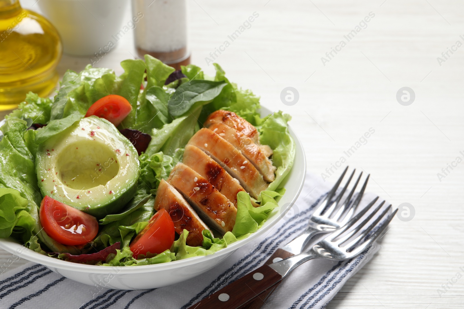 Photo of Delicious salad with chicken, cherry tomato and avocado served on white wooden table, closeup. Space for text