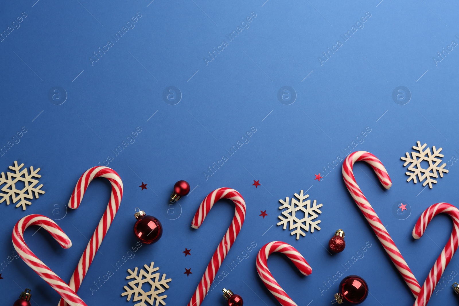 Photo of Candy canes, Christmas balls and snowflakes on blue background, flat lay. Space for text