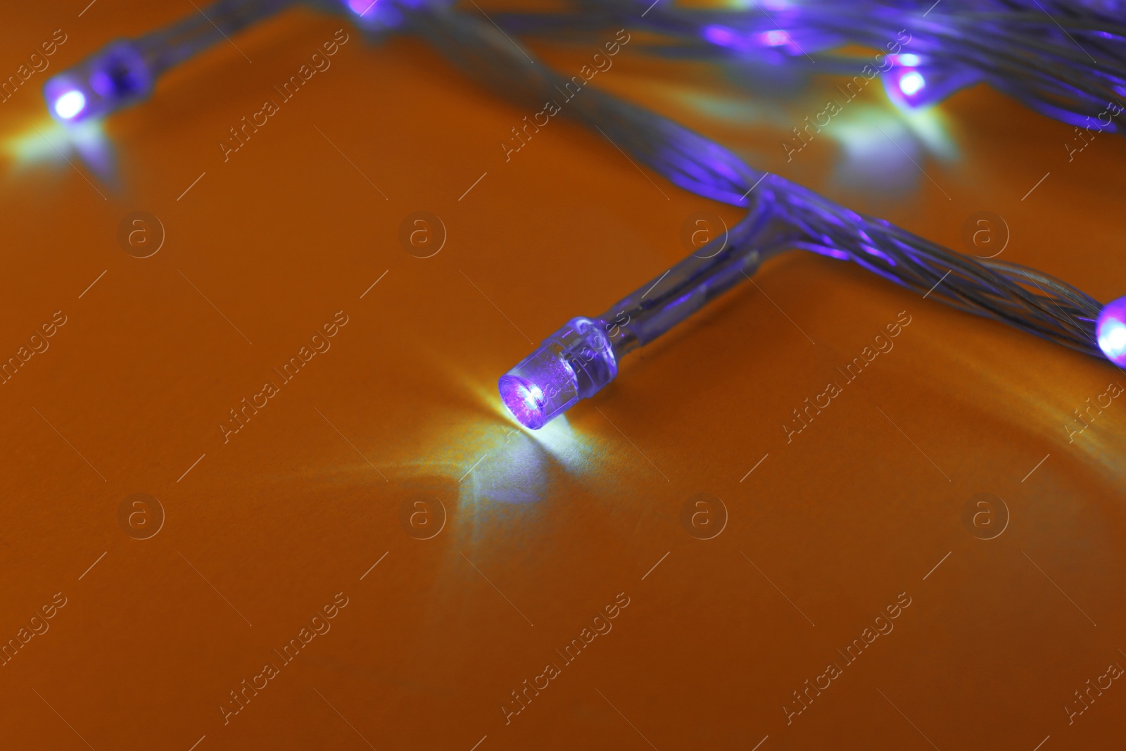 Photo of Glowing Christmas lights on yellow background, closeup