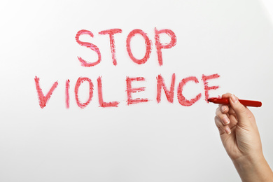 Photo of Woman writing phrase STOP VIOLENCE on glass against white background, closeup