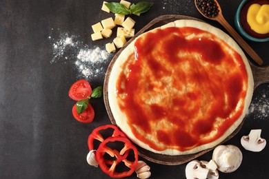 Photo of Pizza dough smeared with tomato sauce and products on dark table, flat lay. Space for text