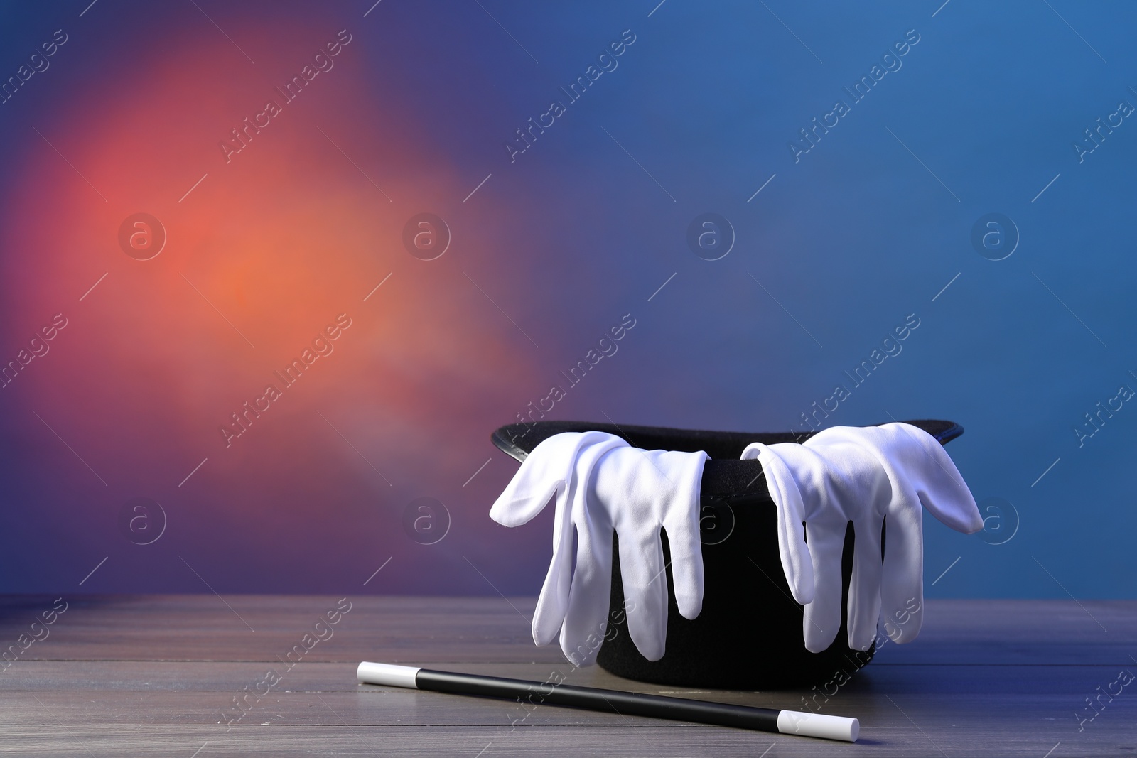 Photo of Magician's hat, wand and gloves on wooden table against color background, space for text