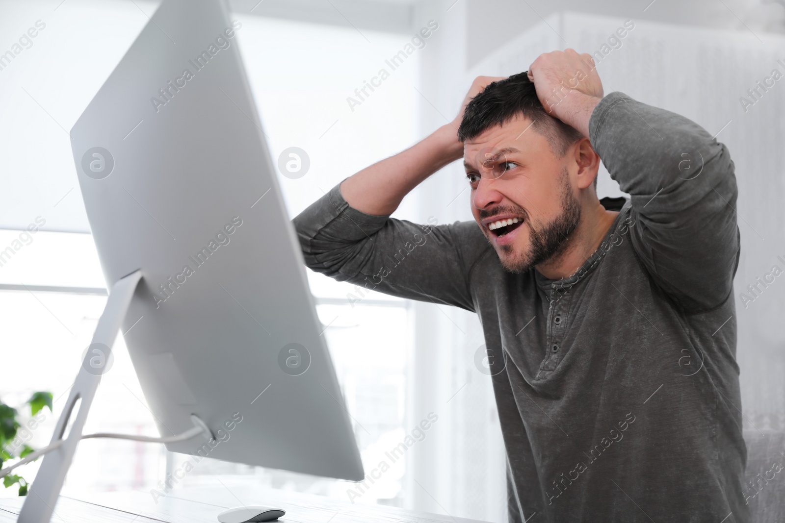 Photo of Emotional man in front of computer at workplace. Online hate concept