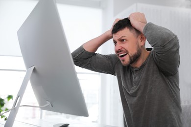 Photo of Emotional man in front of computer at workplace. Online hate concept