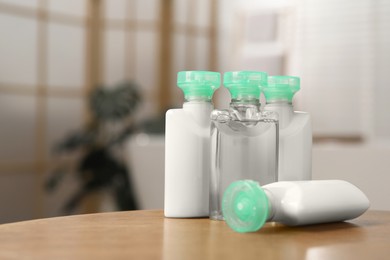 Mini bottles of cosmetic products on wooden table against blurred background. Space for text