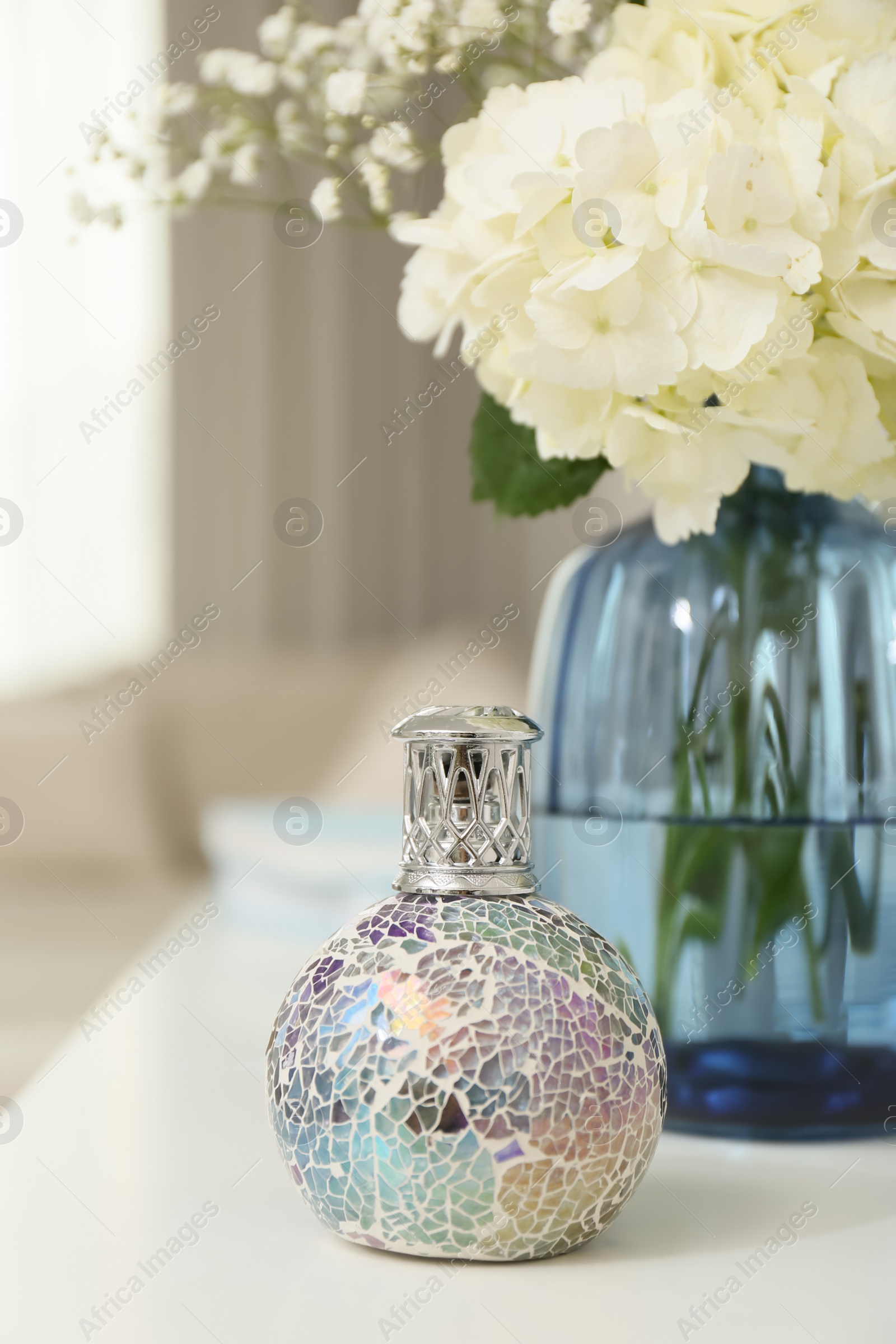 Photo of Stylish catalytic lamp with beautiful bouquet on white table in living room. Cozy interior