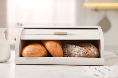 Photo of Wooden bread basket with freshly baked loaves on white marble table in kitchen