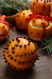 Photo of Pomander balls made of tangerines with cloves and fir branches on wooden table, closeup