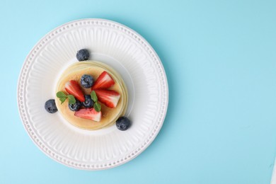 Photo of Delicious pancakes with strawberries, blueberries and mint on light blue background, top view. Space for text