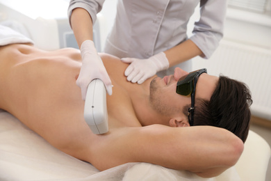 Photo of Young man undergoing laser epilation procedure in beauty salon