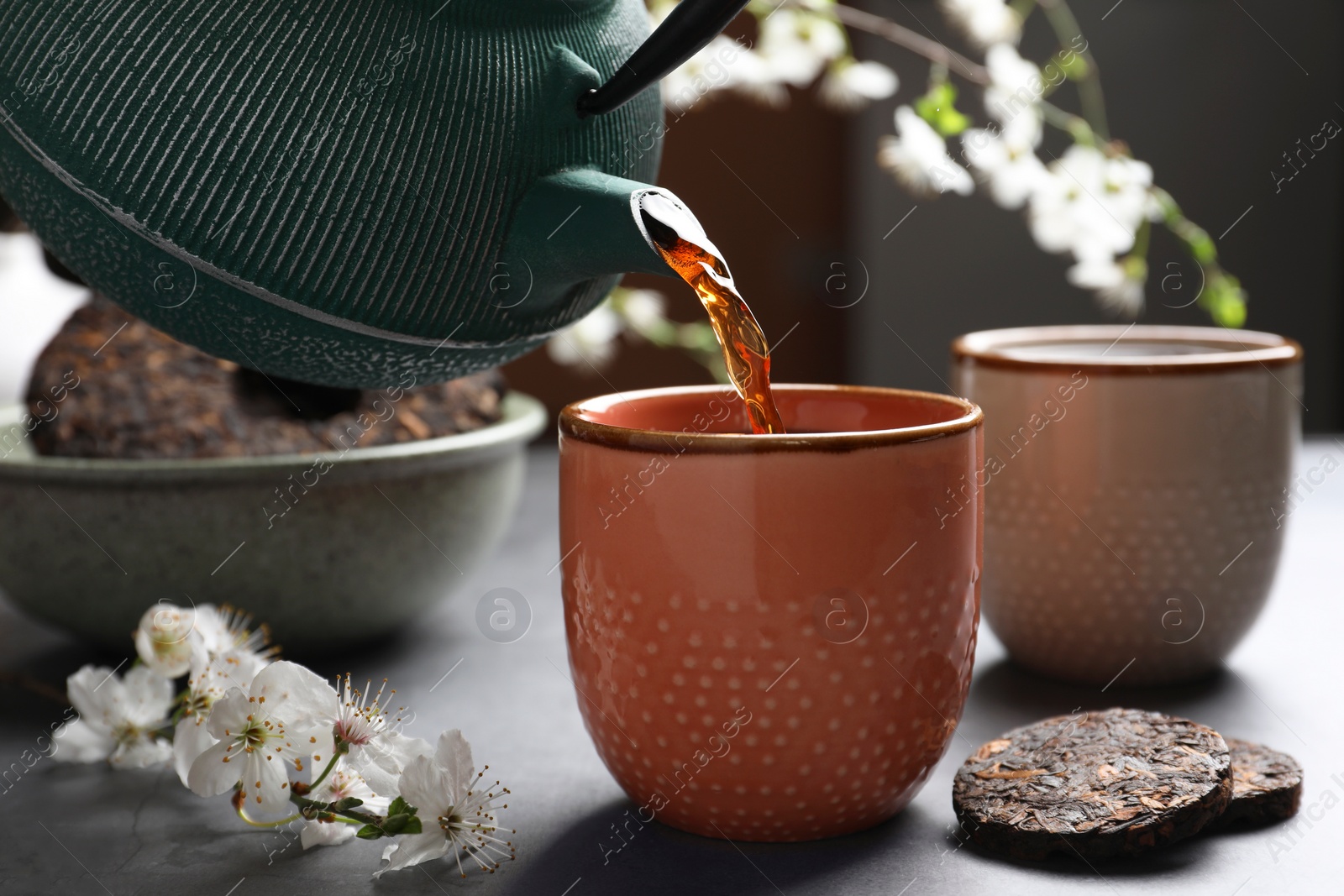 Photo of Pouring freshly brewed pu-erh tea into cup on grey table, closeup