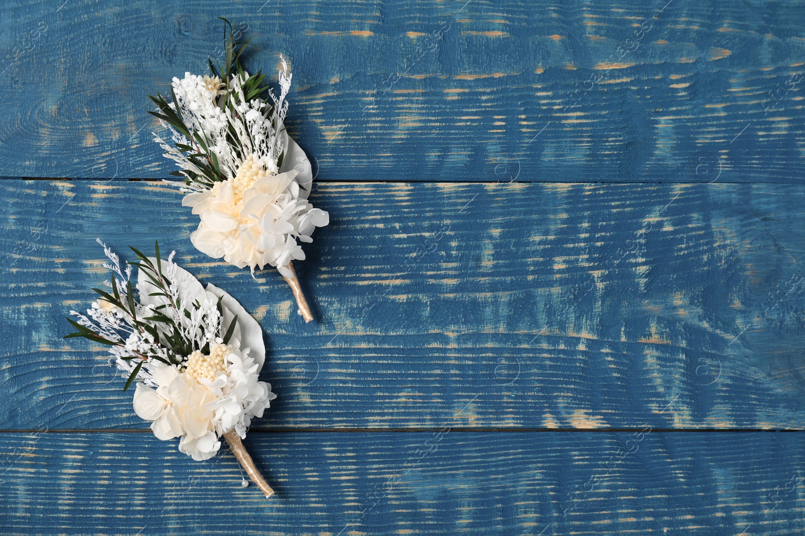 Photo of Stylish white boutonnieres on blue wooden table, top view. Space for text