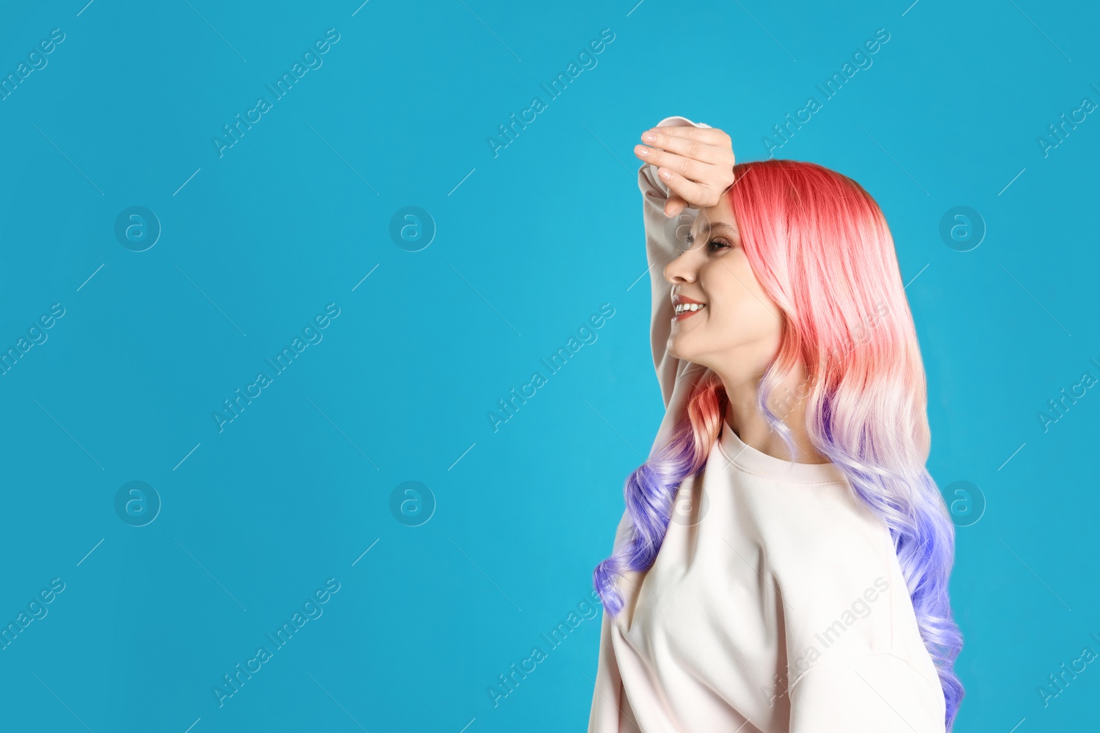 Image of Portrait of young woman with dyed long curly hair on blue background, space for text