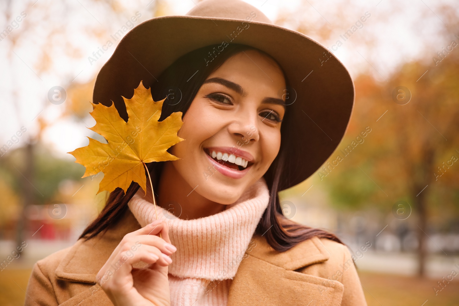 Photo of Young woman in stylish clothes holding yellow leaf outdoors. Autumn look