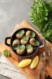 Photo of Delicious cooked snails in baking dish served on grey textured table, flat lay