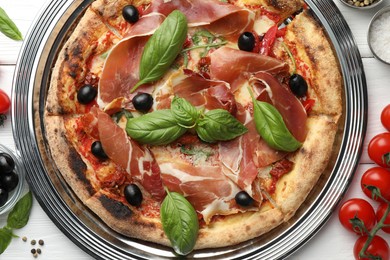 Tasty pizza with cured ham, olives, tomatoes and basil on white wooden table, flat lay