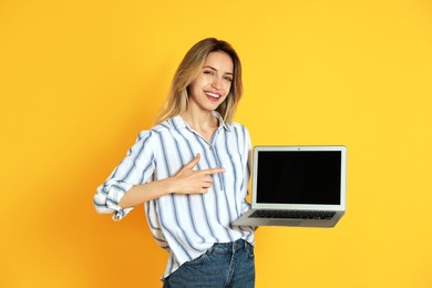 Young woman with modern laptop on yellow background