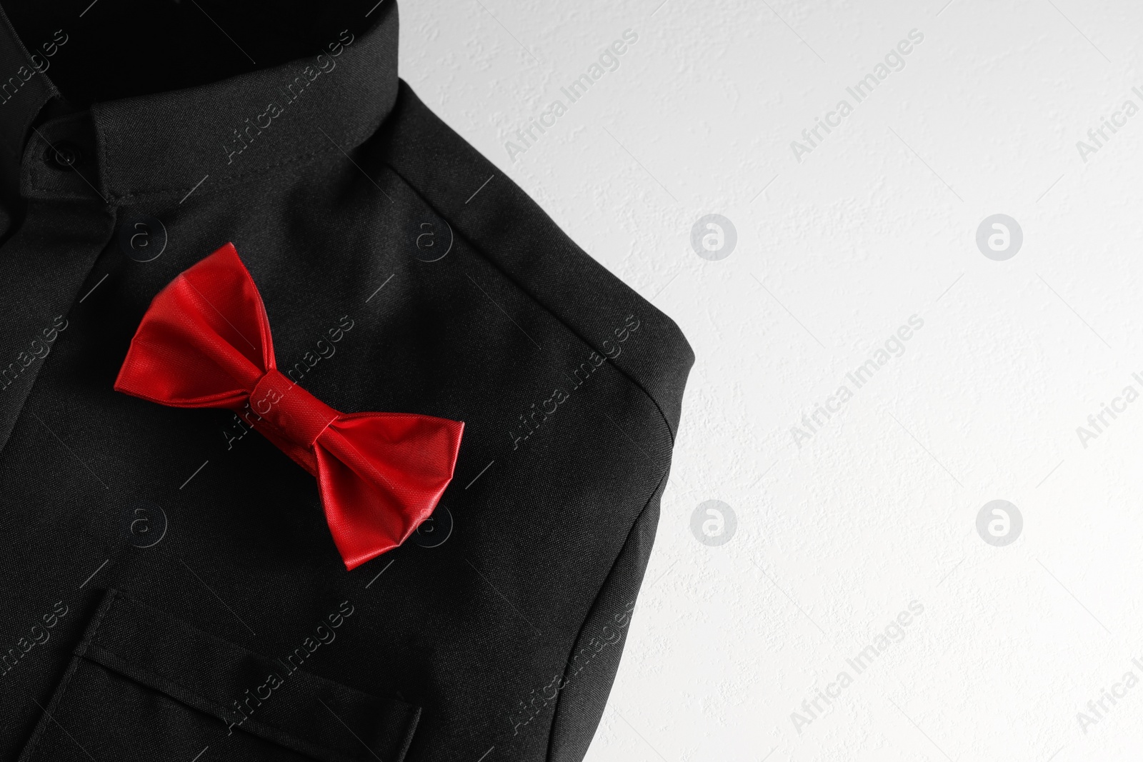 Photo of Black shirt with stylish red bow tie on white background, space for text