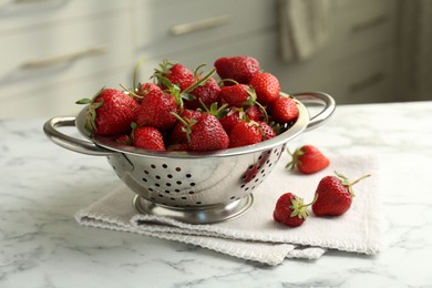 Photo of Metal colander with fresh strawberries on white marble table in kitchen