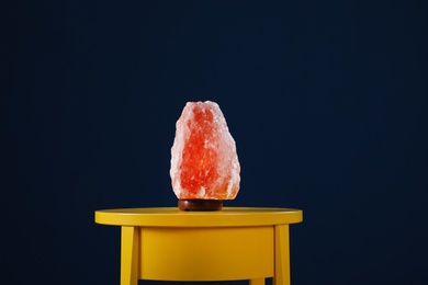 Himalayan salt lamp on yellow table against dark blue background