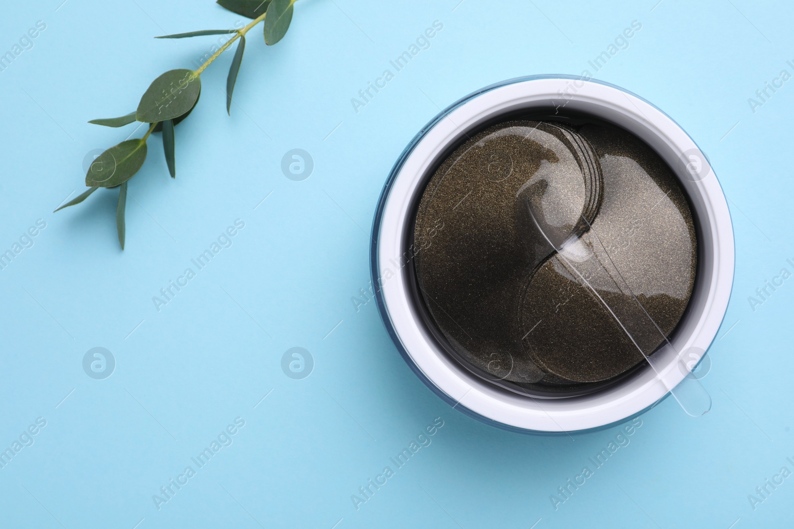 Photo of Under eye patches in jar with spatula and green twig on light blue background, flat lay. Cosmetic product