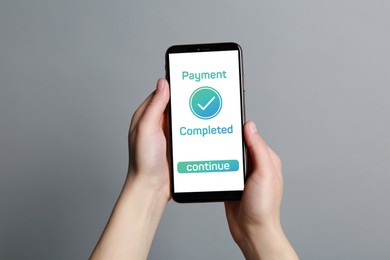 Woman successfully made payment using online banking application on smartphone on grey background, closeup