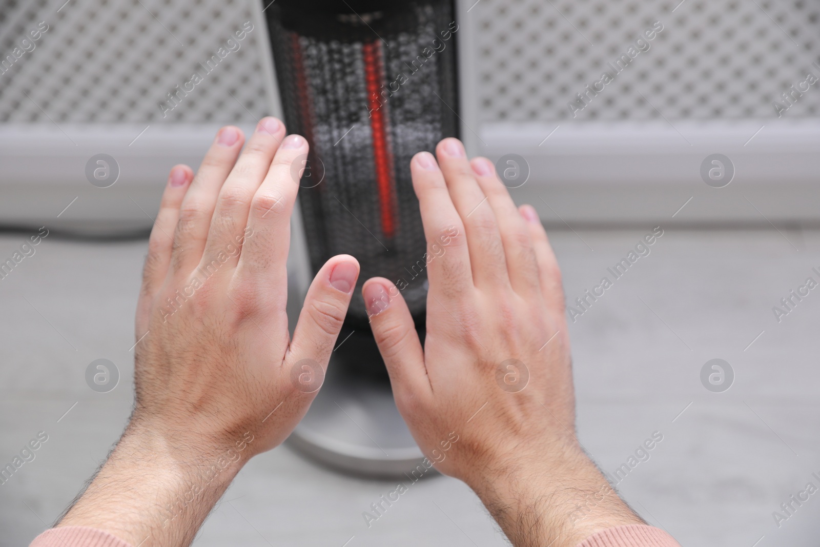 Photo of Man warming hands near modern heater indoors, closeup