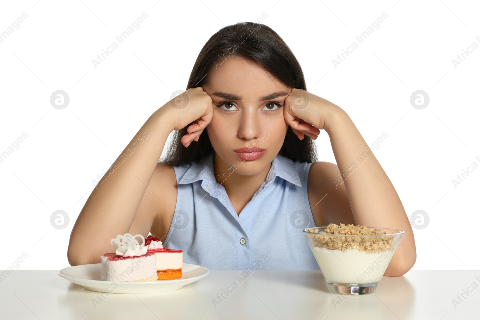 Photo of Doubtful woman choosing between yogurt with granola and cake at table on white background