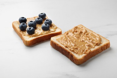 Photo of Delicious toasts with peanut butter and blueberries on white marble table, closeup