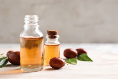 Glass bottles with jojoba oil and seeds on light table against grey background. Space for text