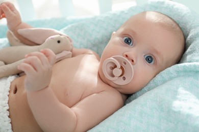 Cute little baby with pacifier and toy bunny lying in crib