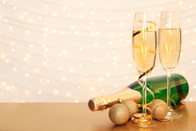 Photo of Christmas balls, glasses and bottle of champagne on table against blurred lights