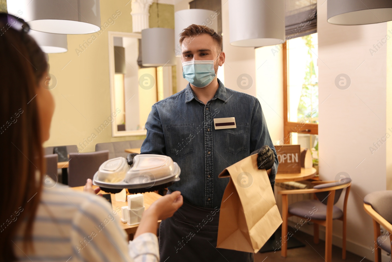 Photo of Waiter giving packed takeout order to customer in restaurant. Food service during coronavirus quarantine