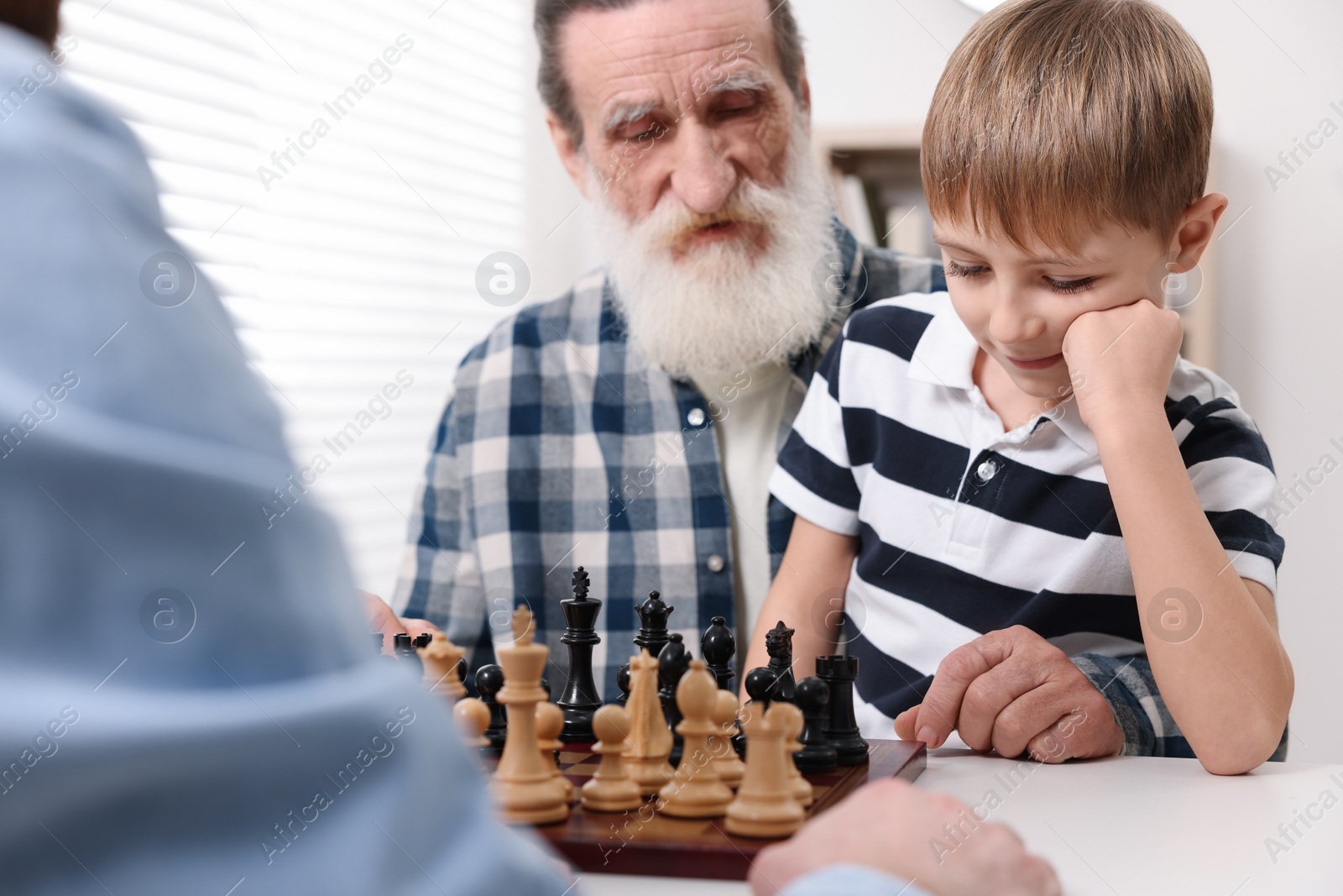 Photo of Family playing chess together at table in room