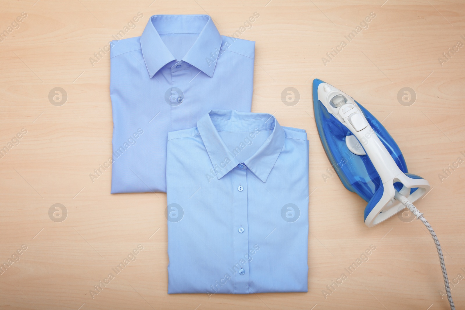 Photo of Folded clean clothes and iron on wooden background, top view