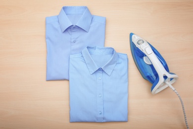 Photo of Folded clean clothes and iron on wooden background, top view