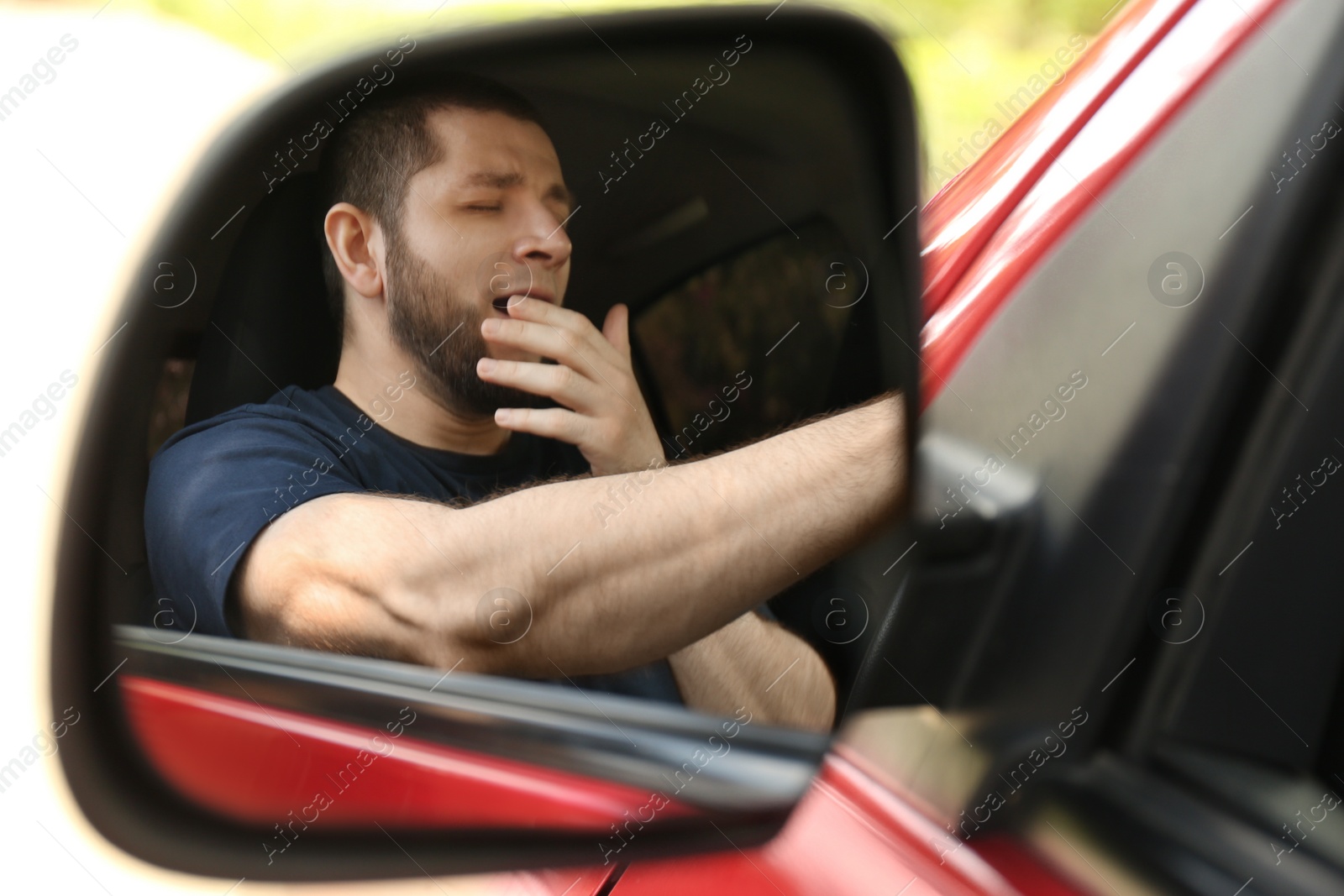 Photo of Tired man yawning in his auto, view through car side mirror