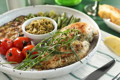 Photo of Tasty chicken, vegetables with tarragon and pesto sauce served on table, closeup