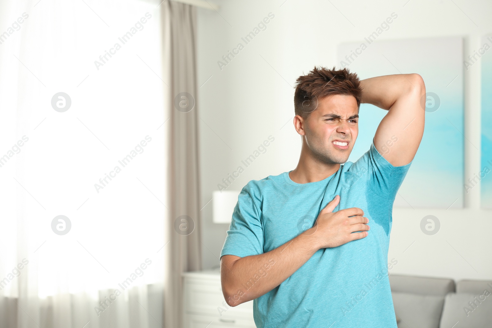 Photo of Young man with sweat stain on his clothes indoors, space for text. Using deodorant