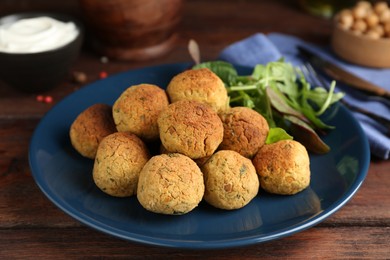 Photo of Delicious falafel balls with herbs on wooden table, closeup