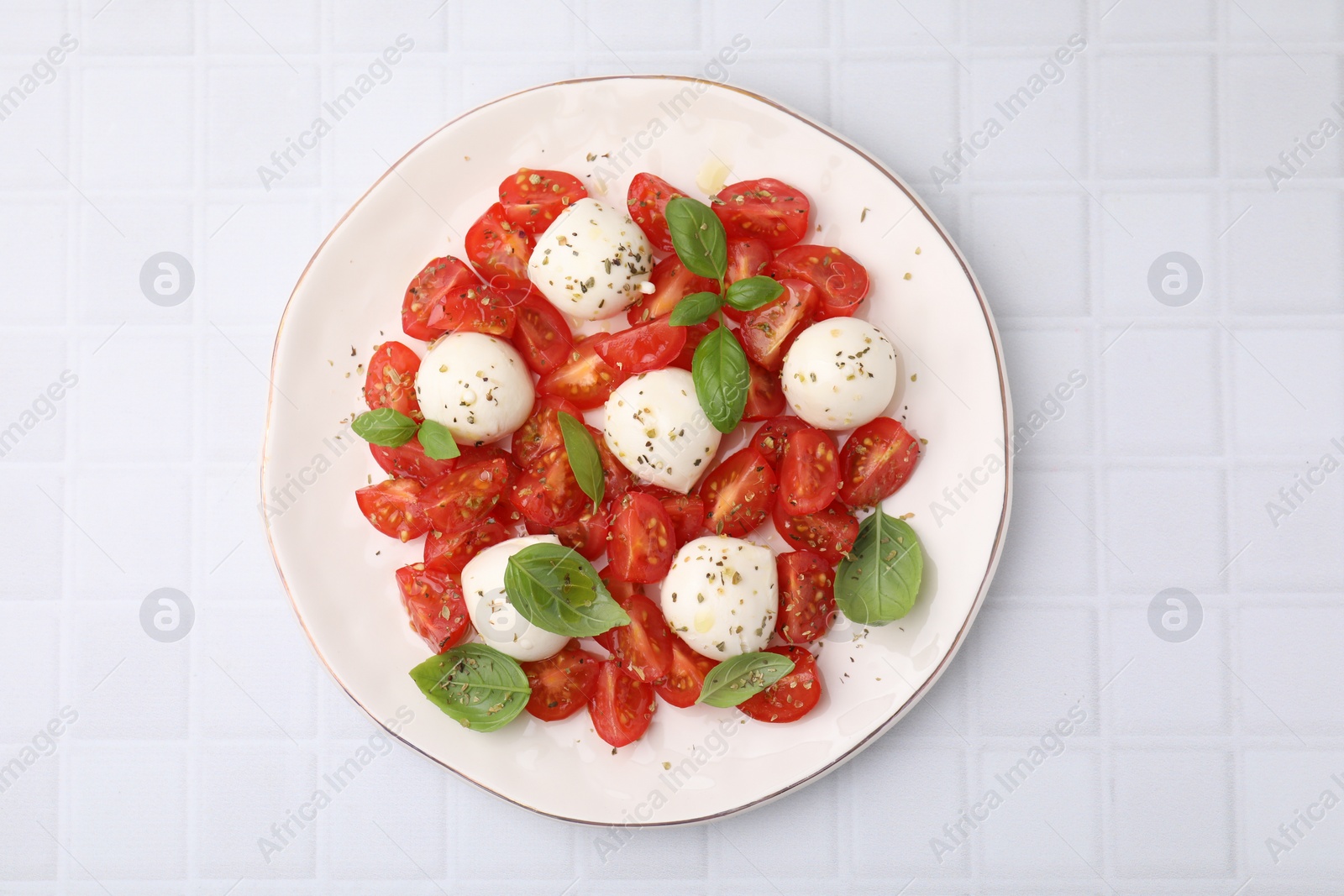 Photo of Tasty salad Caprese with tomatoes, mozzarella balls and basil on white tiled table, top view