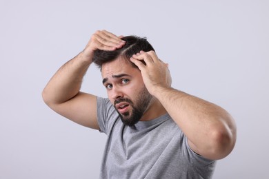 Emotional man examining his head on light grey background. Dandruff problem