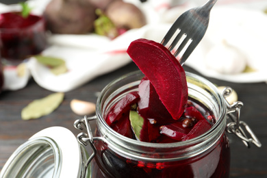 Fork with pickled beet over glass jar on wooden table, closeup