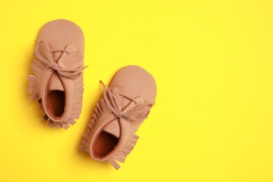 Cute baby shoes on yellow background, flat lay. Space for text