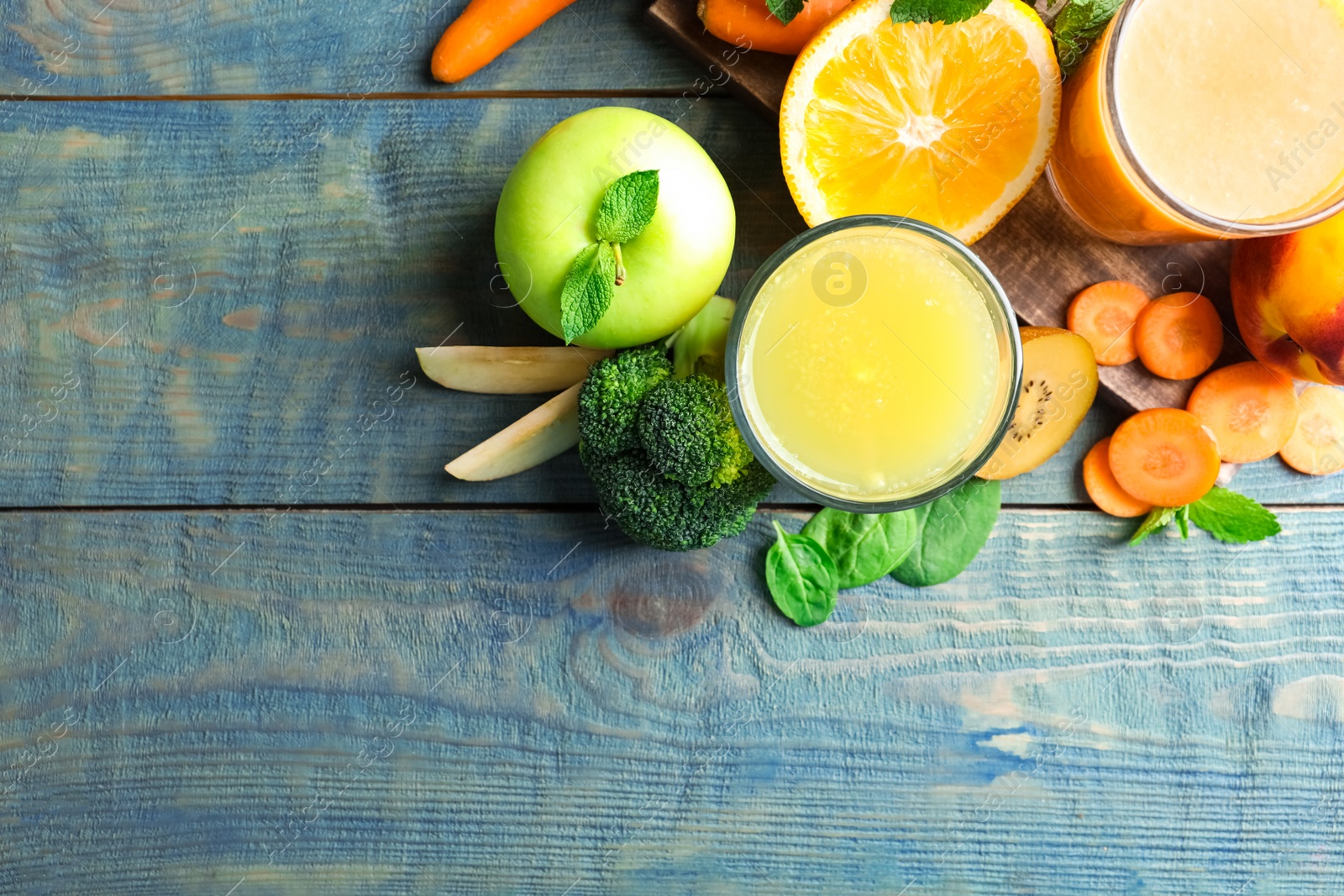 Photo of Glasses of delicious juices and fresh ingredients on blue wooden table, flat lay. Space for text