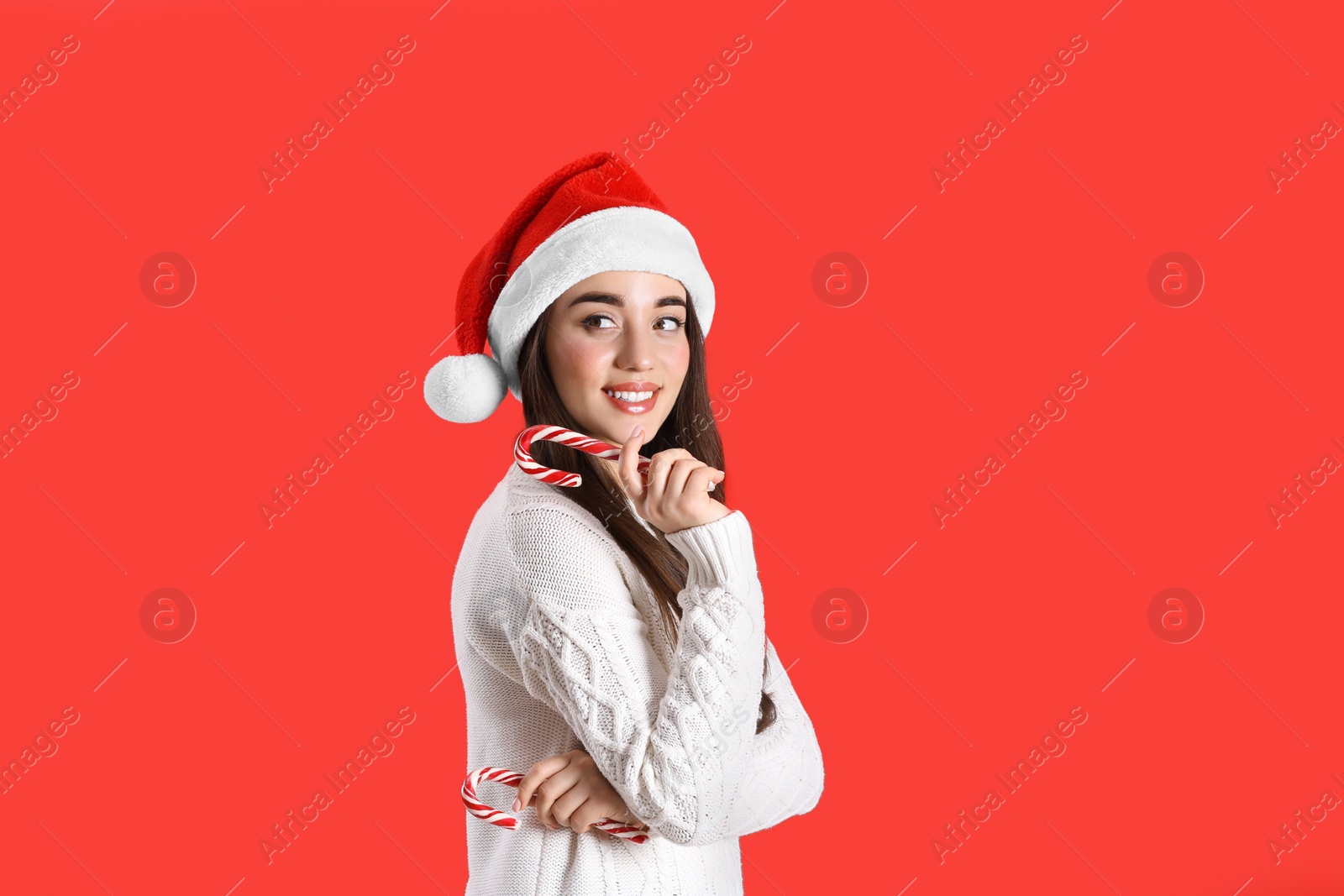 Photo of Beautiful woman in Santa Claus hat holding candy cane on red background